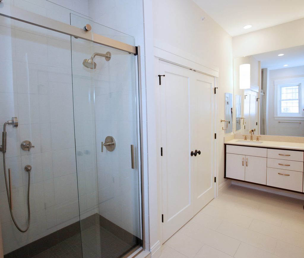 A glass barn door shower enclosure adds form and functionality to this stunning bathroom. Behind those doors are a washer and dryer. 